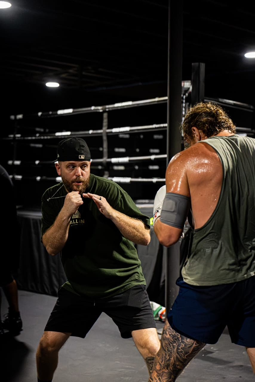 Coach Kevin Gleason holding a guard and talking a boxer through it beside the ring.