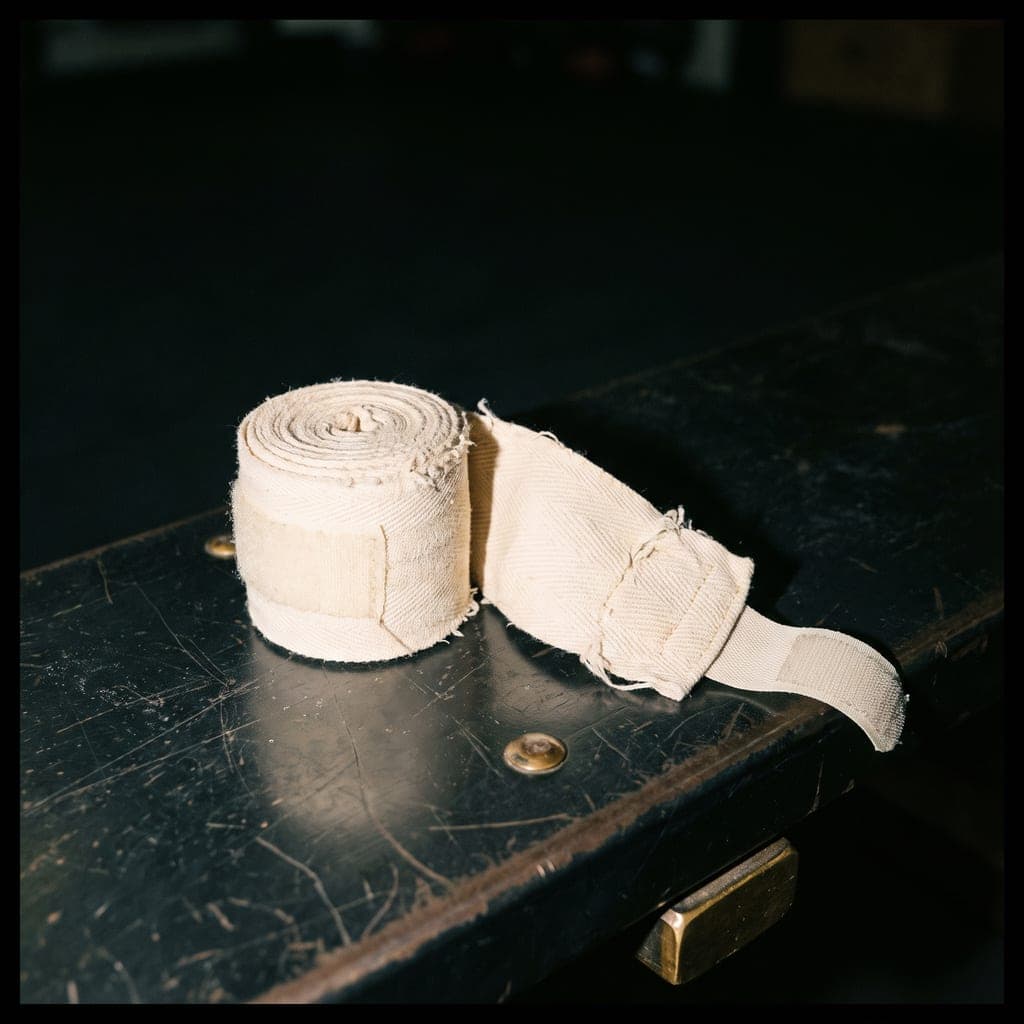 Two rolled ivory cotton hand wraps resting on a dark steel bench, lit by direct flash.