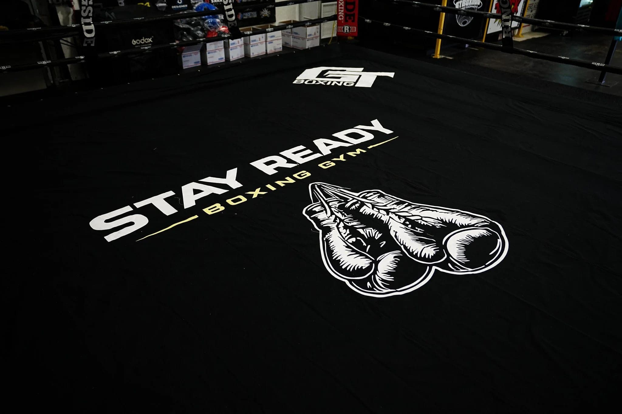 The Stay Ready Boxing Gym ring, its logo printed across the black canvas, seen from a corner under low light.